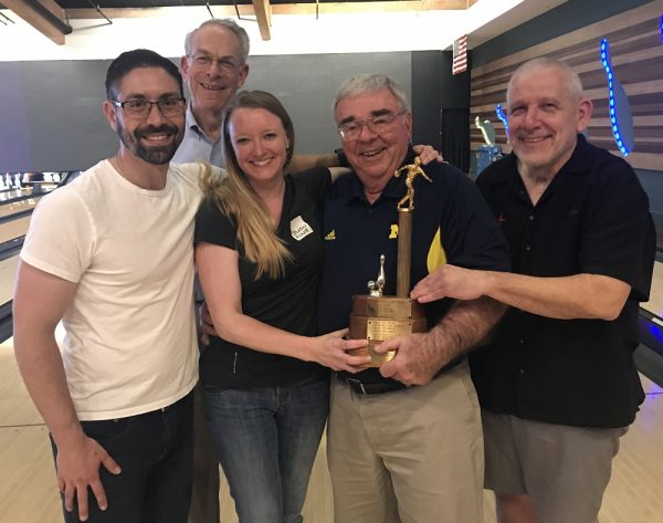 A group of four men and one woman smiling and holding a trophy.