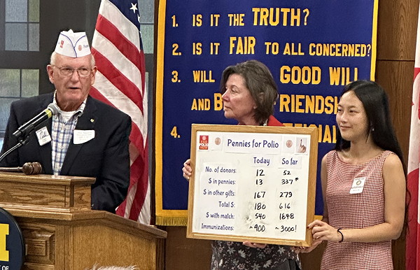 Two women holding a bulletin board, while a man explains.
